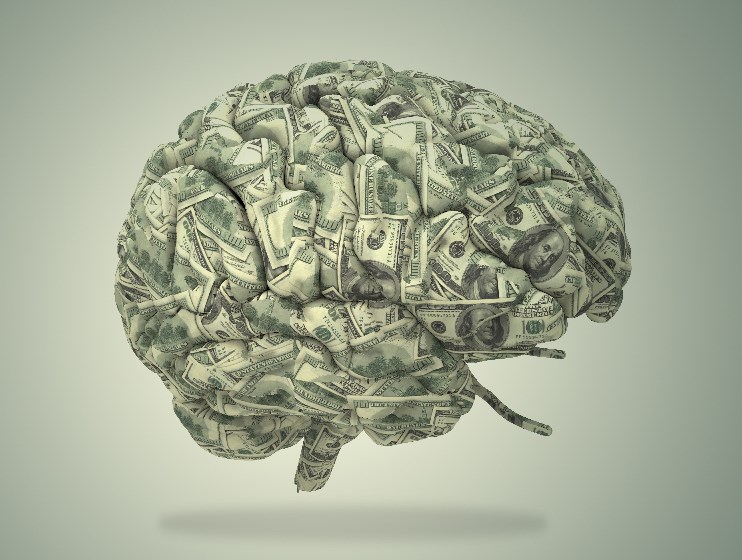 A photo of a human brain sculpted out of $100 bills on a green background.
