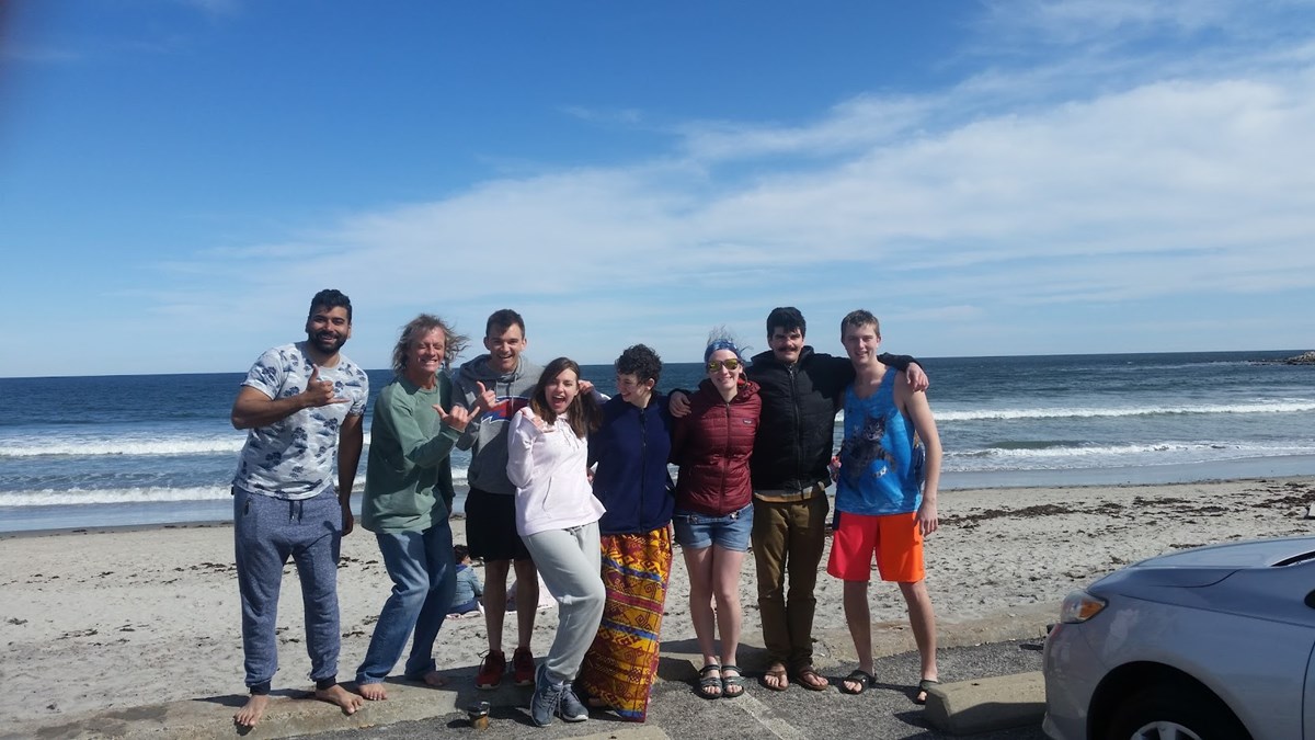 A group of UMass Lowell students stand smiling in front of the ocean surf.