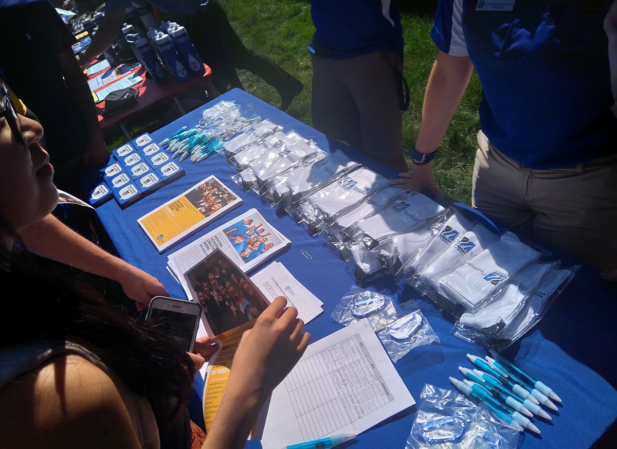 A table displaying UMass Lowell branded swag including: magnets, shirts pens and more.