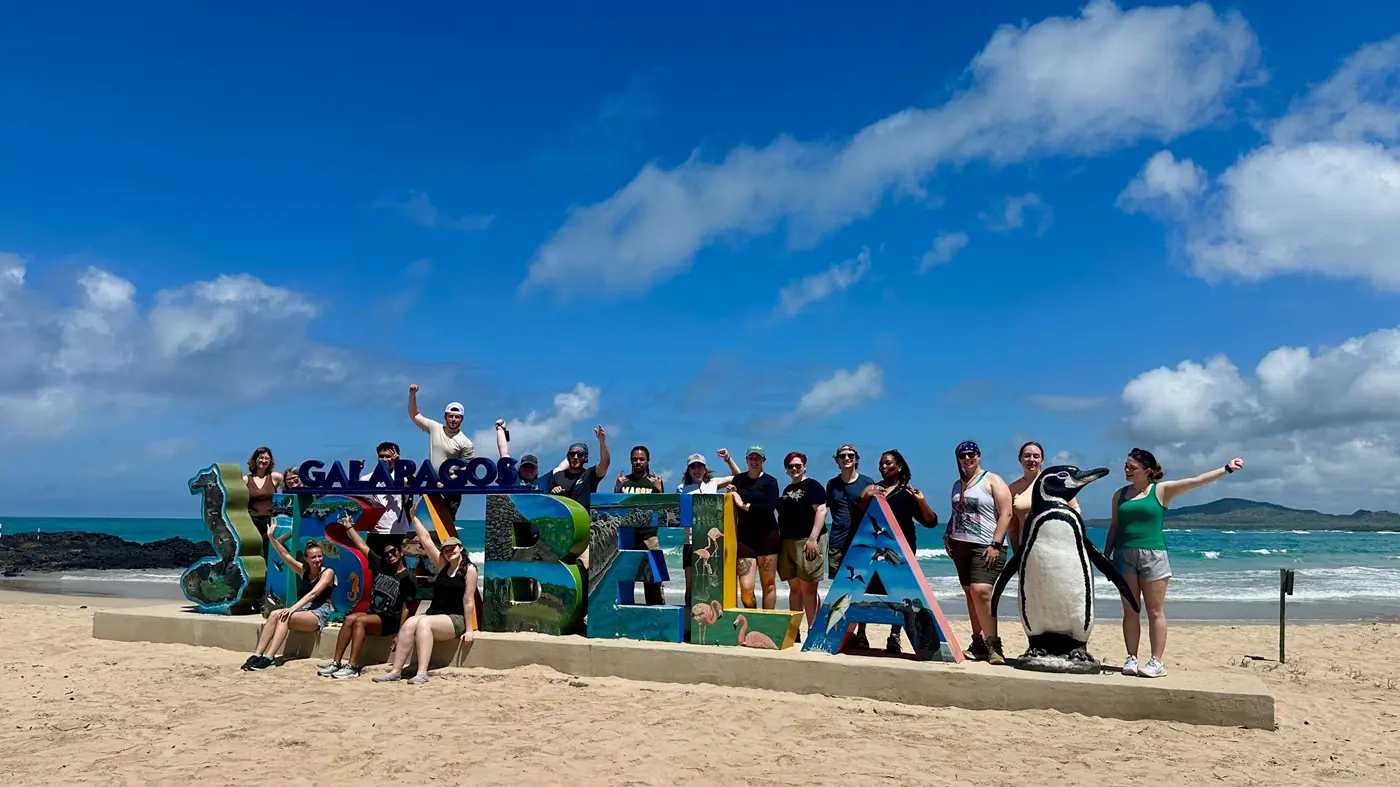 Students hang on Galapagos sign on beach