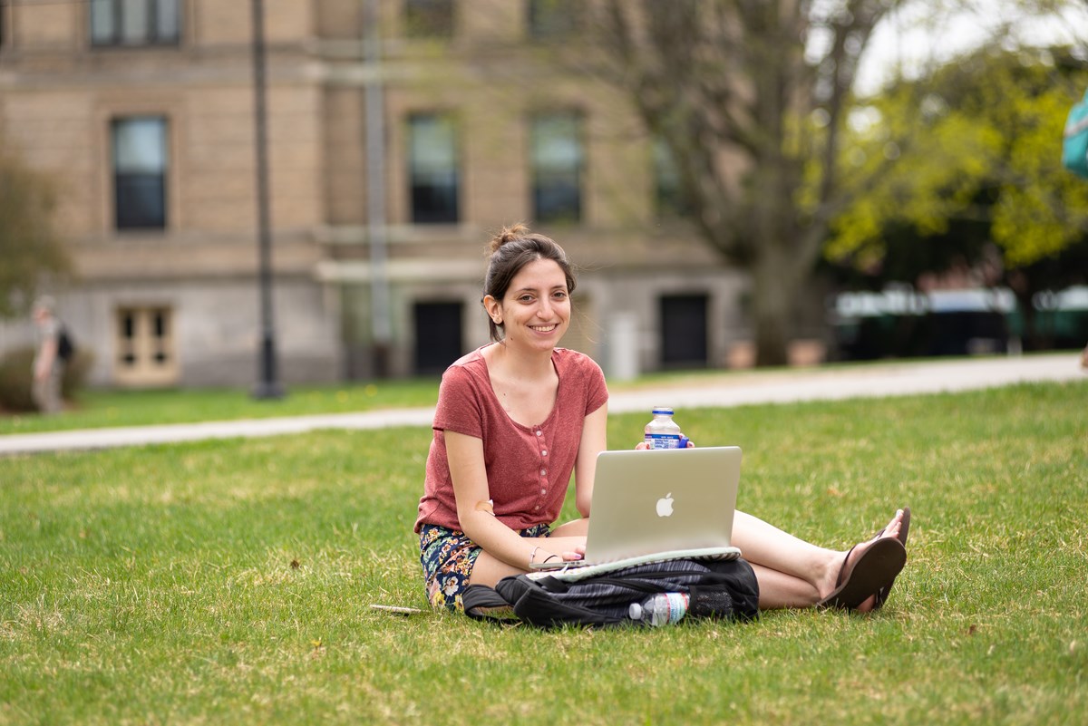 Young woman sitting on grass with laptop on lap