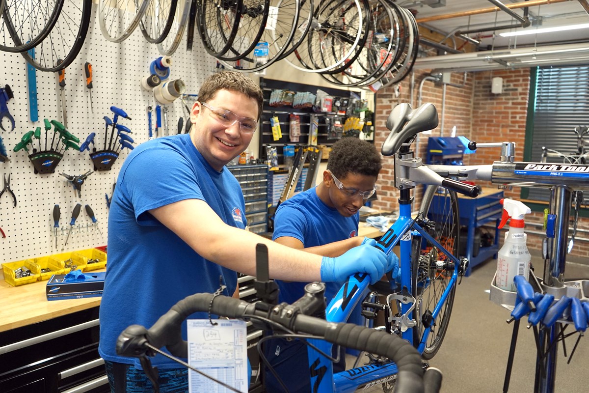 Two smiling student staff members working on a bike