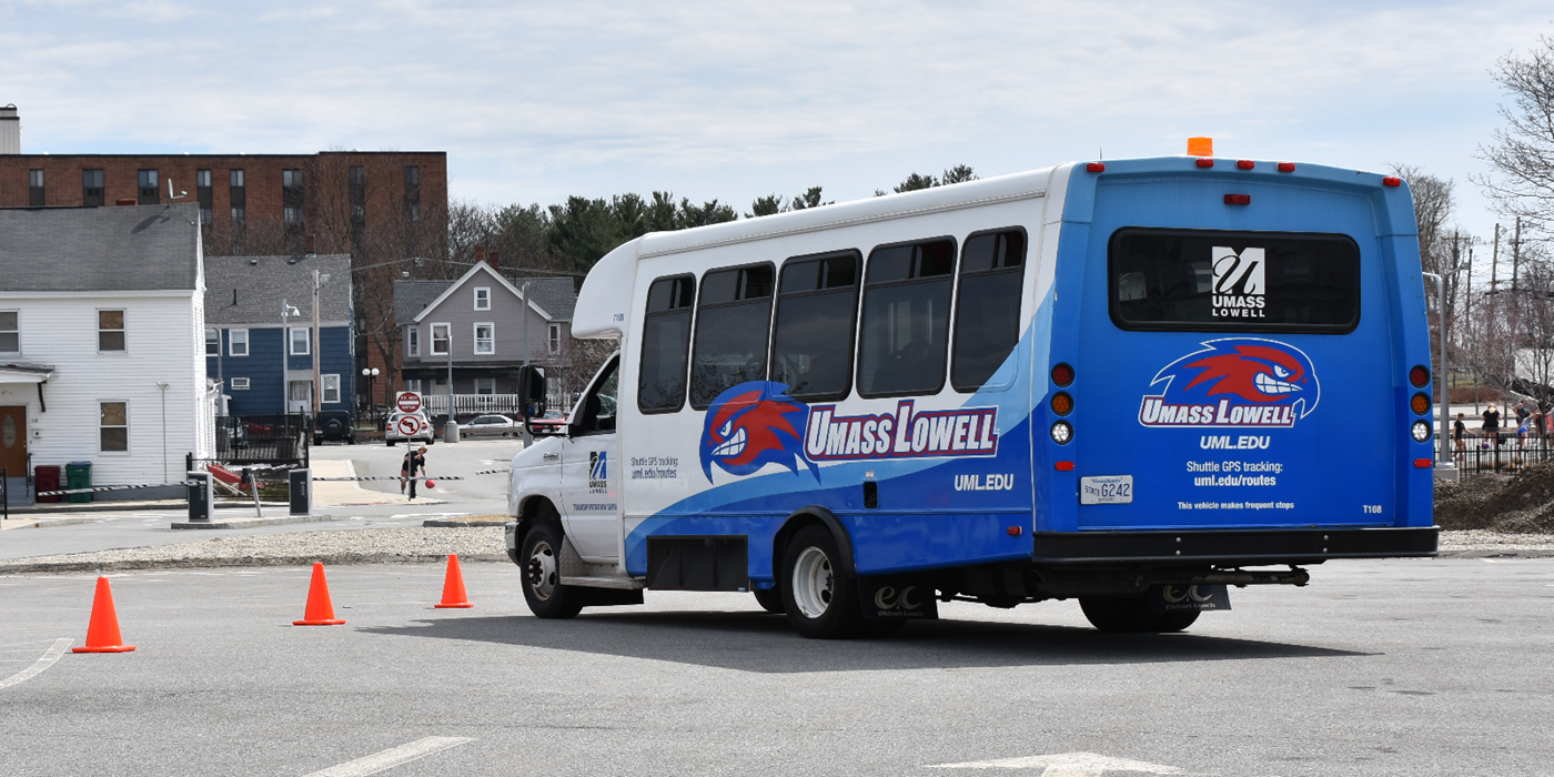 A UMass Lowell shuttle bus reverses in a parking lot
