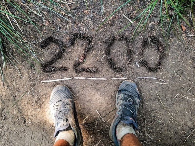 A shot of Kyle Soeltz's sneakers and "2200" written in pinecones at his feet (at mile 2200 of the Pacific Crest Trail)
