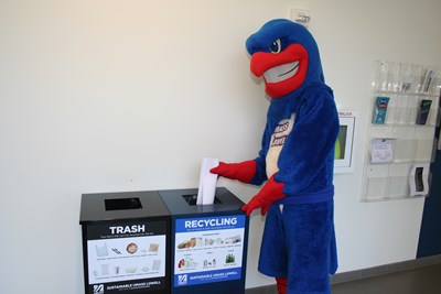 UMass Lowell mascot Rowdy the River Hawk putting paper into a zero-sort recycling bin.