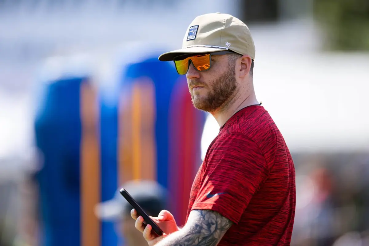 A young man wearing sunglasses and a hat holds a phone while standing outside.