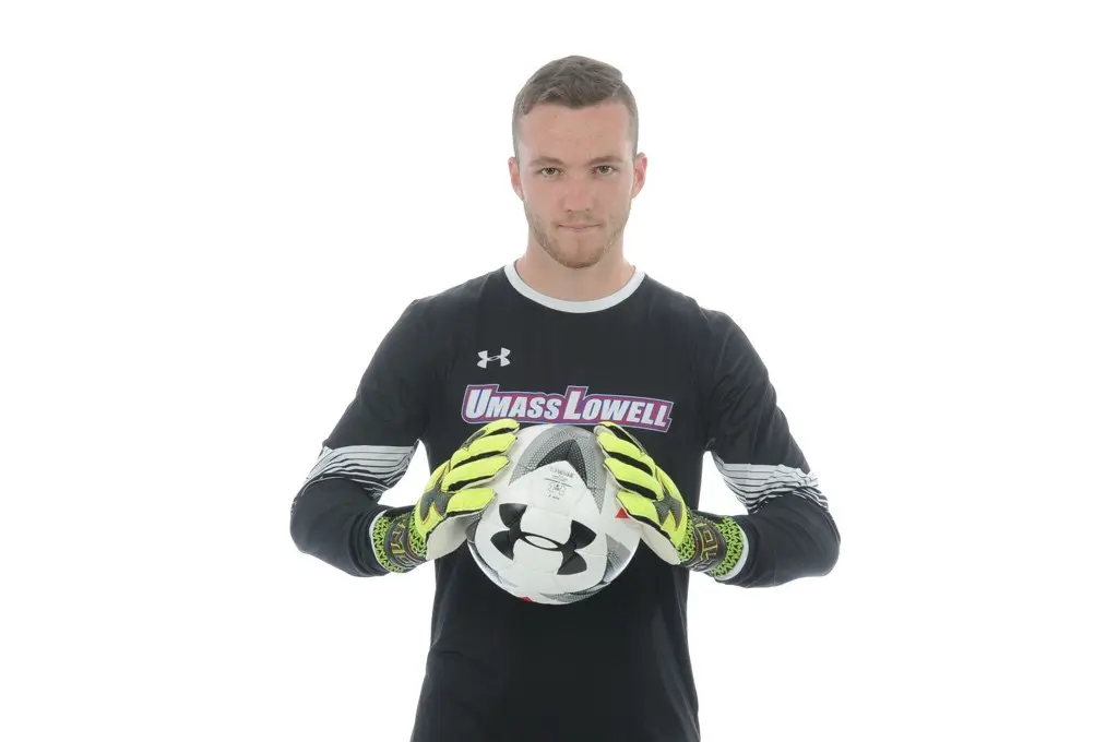 A soccer goalie holds a soccer ball while posing for a photo in front of a white backdrop.