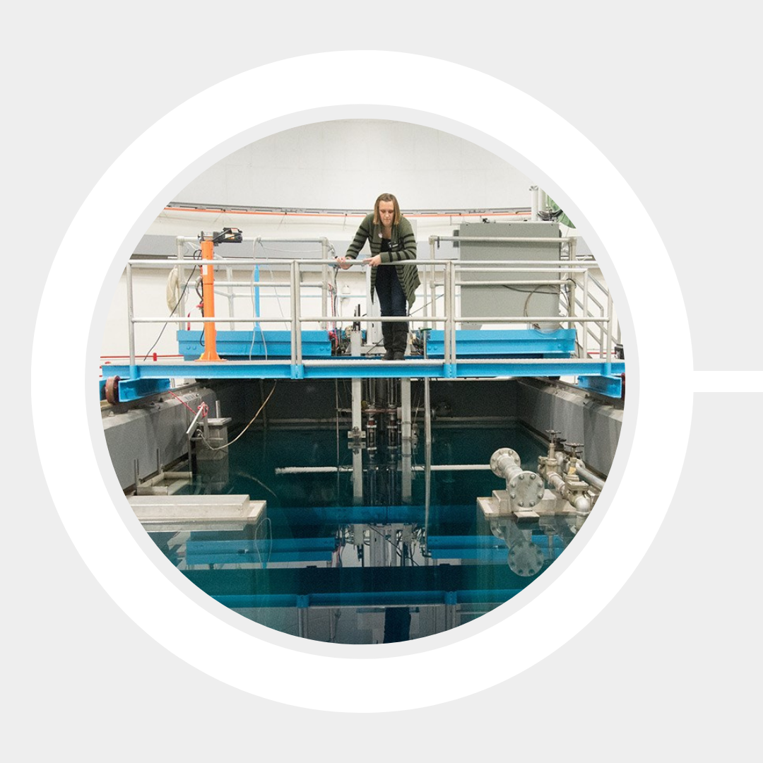 Student standing on a platform above the open-pool nuclear reactor looks down to examine the well.