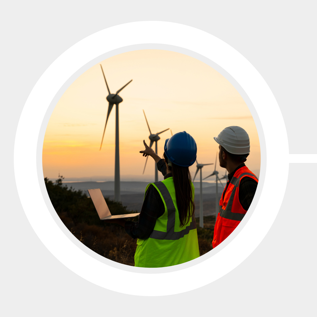 Wind energy technicians in the foreground monitor a wind farm and turbines from their computer.