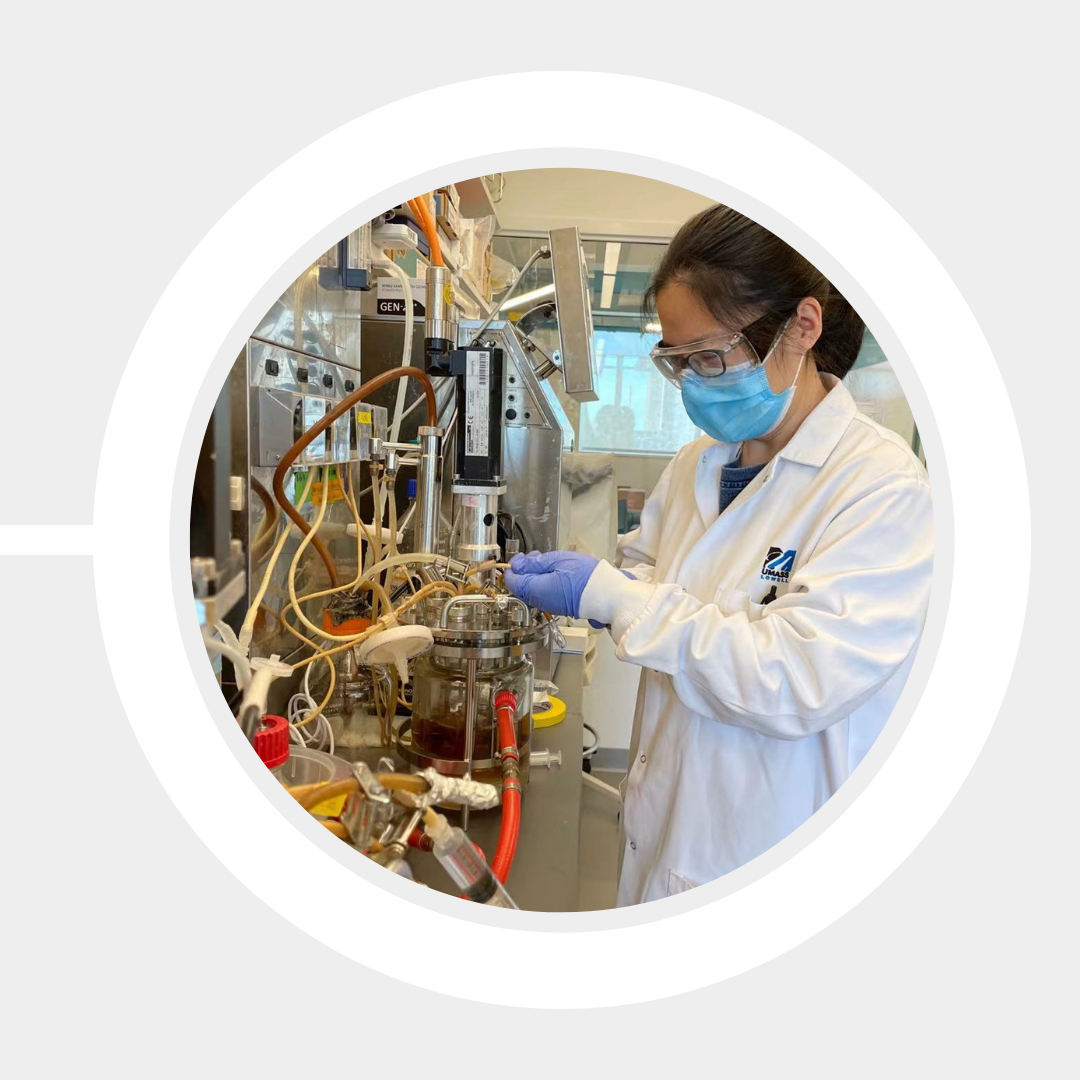 A student wearing protective gear experiments in the lab, connecting hoses to a container of liquid.