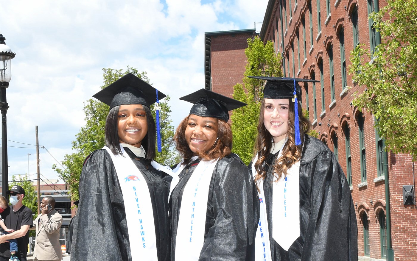 Three female student-athletes in caps and gowns outside 2021 Commencement