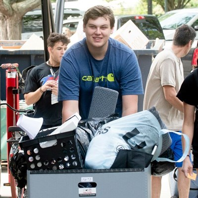 Young man pushing cart full of belongings on move-in day