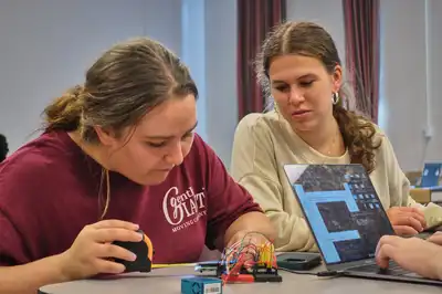 Students examine an electrical component while another enters information on a computer.