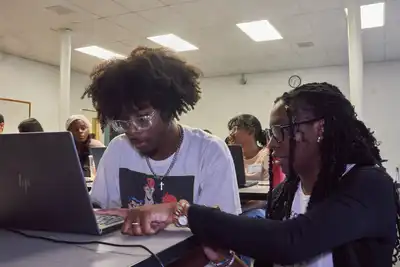 A student indicates something on a laptop computer screen to another student