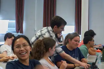 A student laughs in the foreground as an instructor indicates something on a laptop screen for students sitting behind her