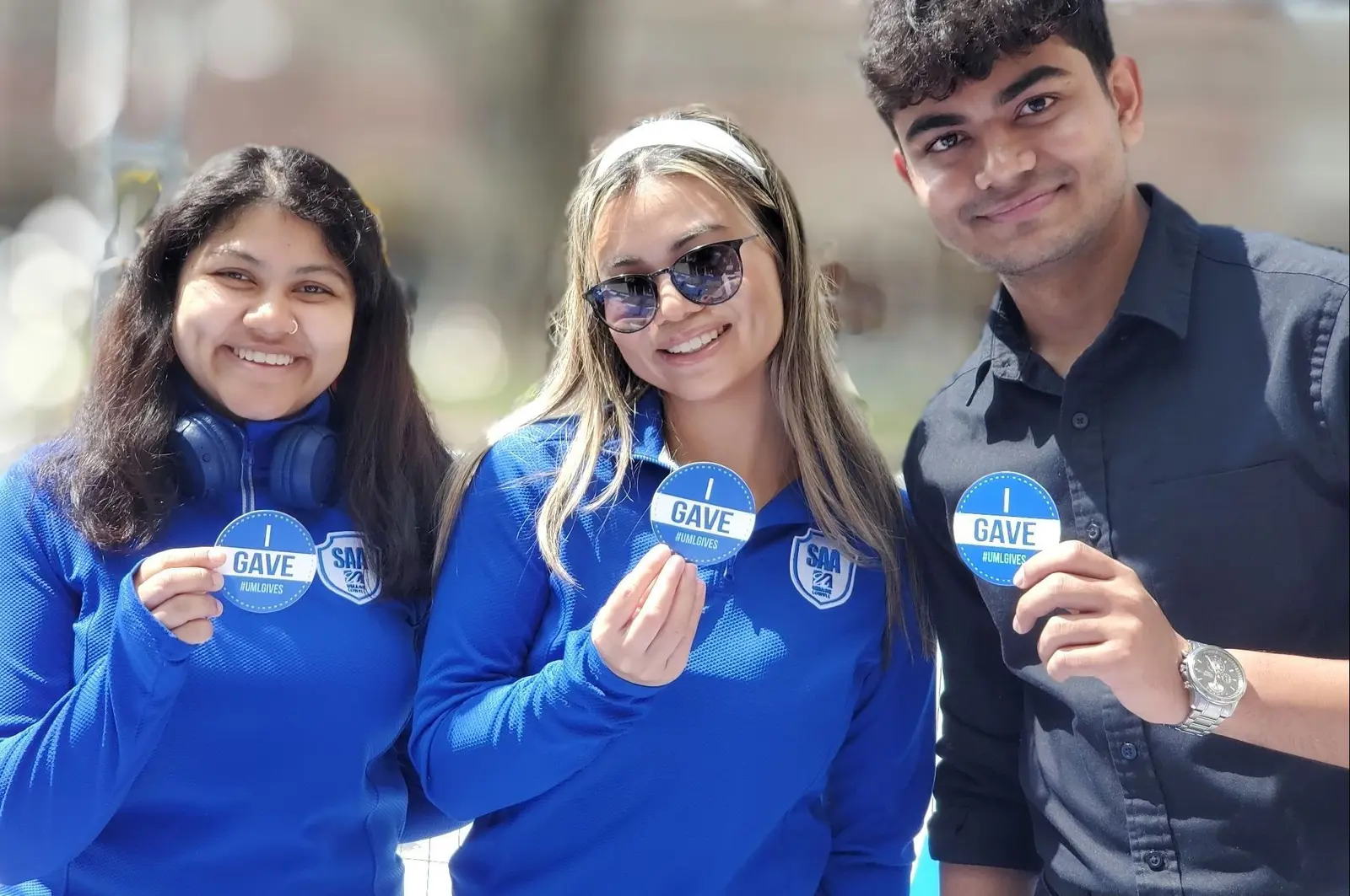 three students hold up I Gave buttons smiling at camera