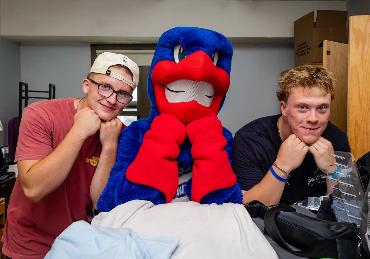 Two roommates flank Rowdy the River Hawk, all with their chins resting on their hands.