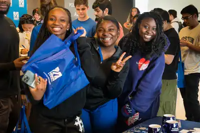 3 students smile and mug for camera while waiting in line