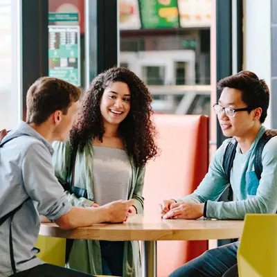 Three students talking at a round table.
