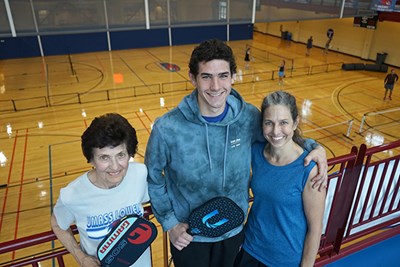 A grandma, grandson and mother pose for a photo with pickleball courts behind them