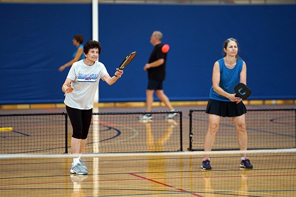 A woman serves during a pickleball game while her teammate stands next to her