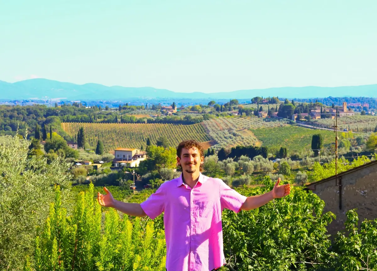 A young man in a pink shirt poses for a photo in Italy.