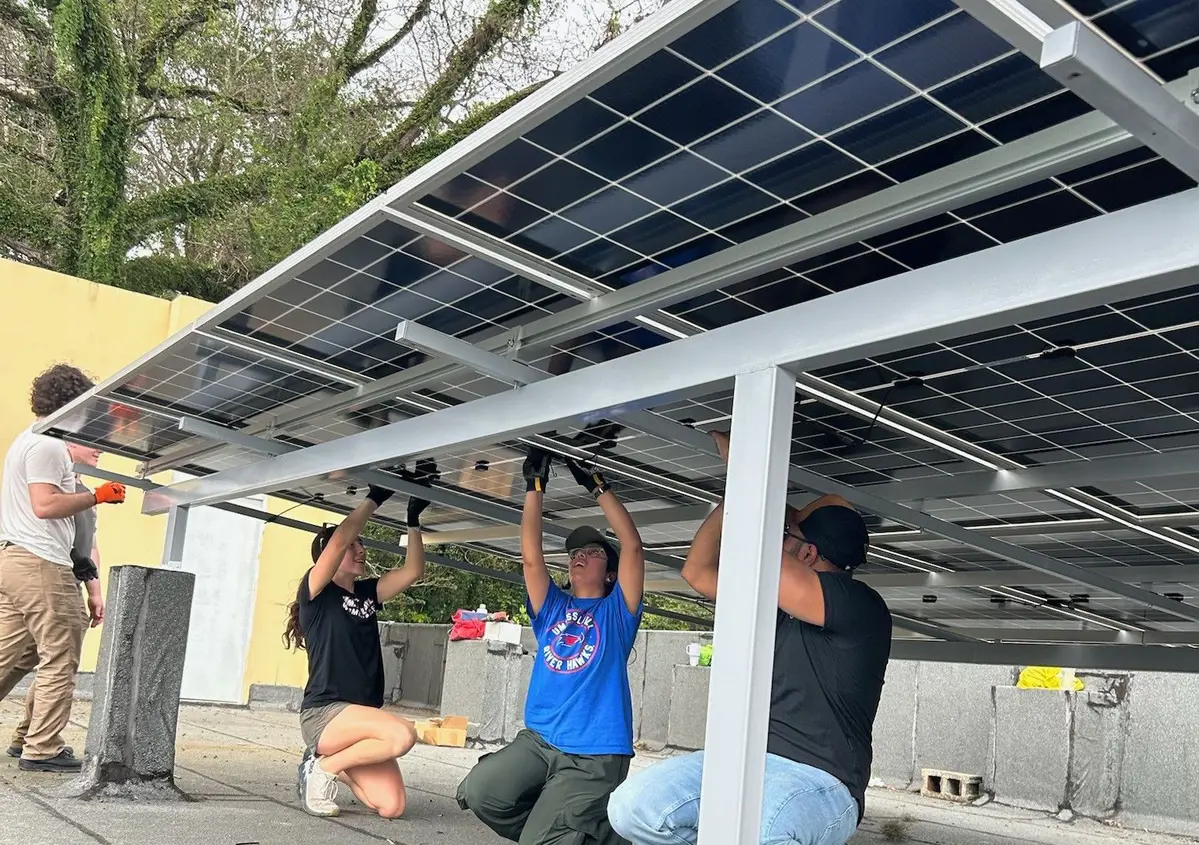 Three students install solar panels from underneath the array.