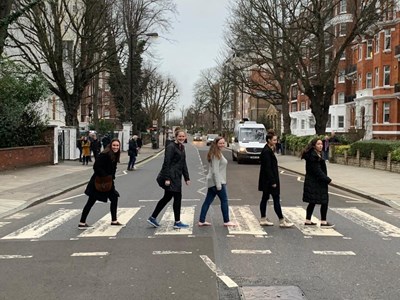 5 students crossing the iconic crosswalk made famous by the Beatles in Abbey Road. There is an album cover with the band crossing this exact crosswalk. It was very crowded and people were running back and forth the busy street trying to capture a photo representing that same cover.