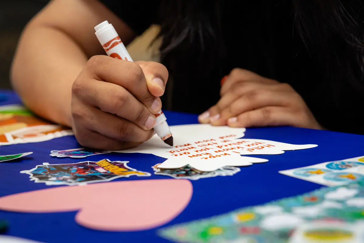 A person writes a note with a marker while sitting at a table.