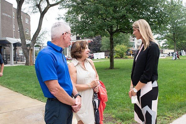 A man in a blue shirt and two women talk outside