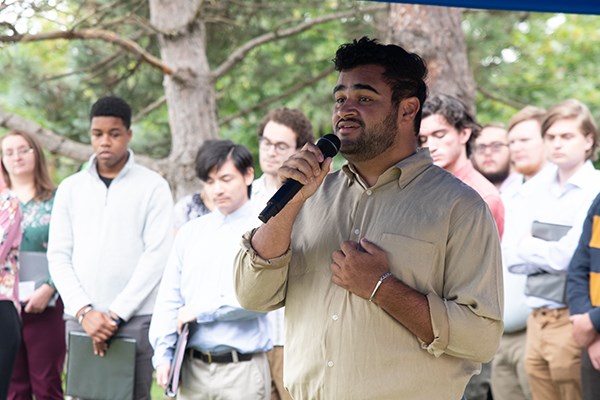 A man holds a microphone and sings while a group of students look on behind him