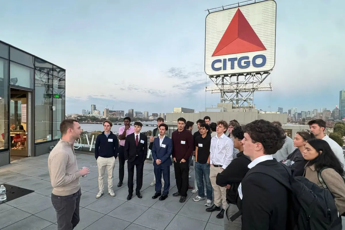 A group of students look at a projection screen while giving a presentation at the front of a room.