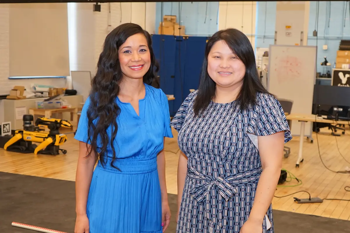 Two women with dark hair pose for a photo while standing in a robotics lab.