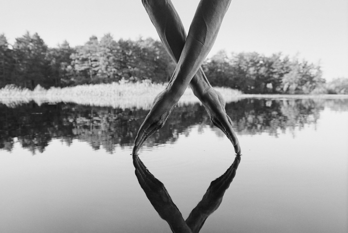 black and white image by Arno Minkkinen of two hands crossed slightly touching the water of a lake