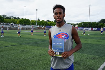 Abdi Shariff-Hassan holds the book "One Goal" on the soccer field
