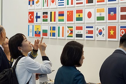 A woman points to a Japanese flag on a wall filled with flags from different countries