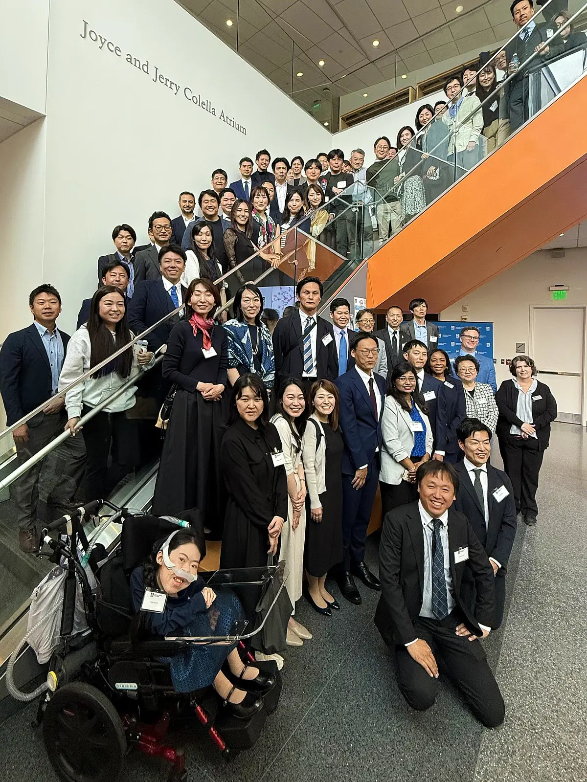 More than 50 people pose for a group photo on the stairs in a building's lobby.