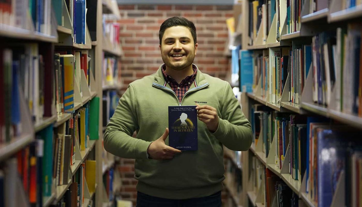 UMass Lowell student holds a book he published titled "There's a Tale In Between"
