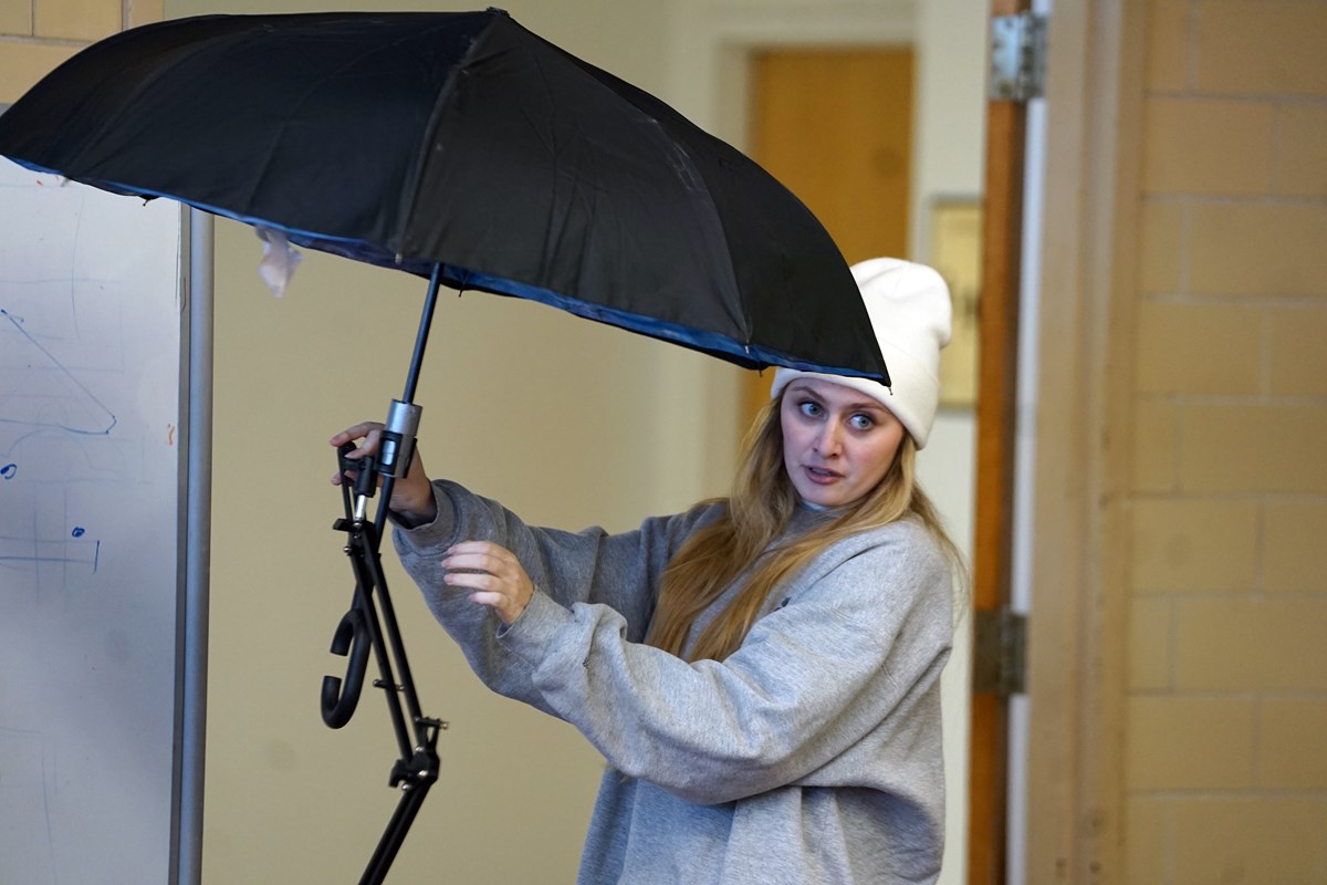 A young woman in a white cap demonstrates a device that is holding an open black umbrella.