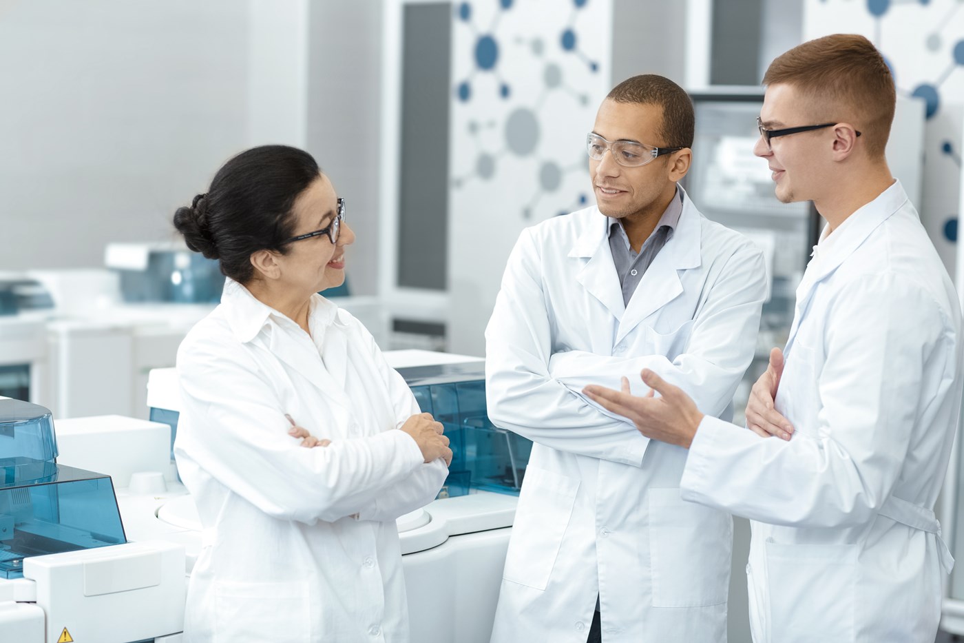 A woman and two men in white lab coats chat