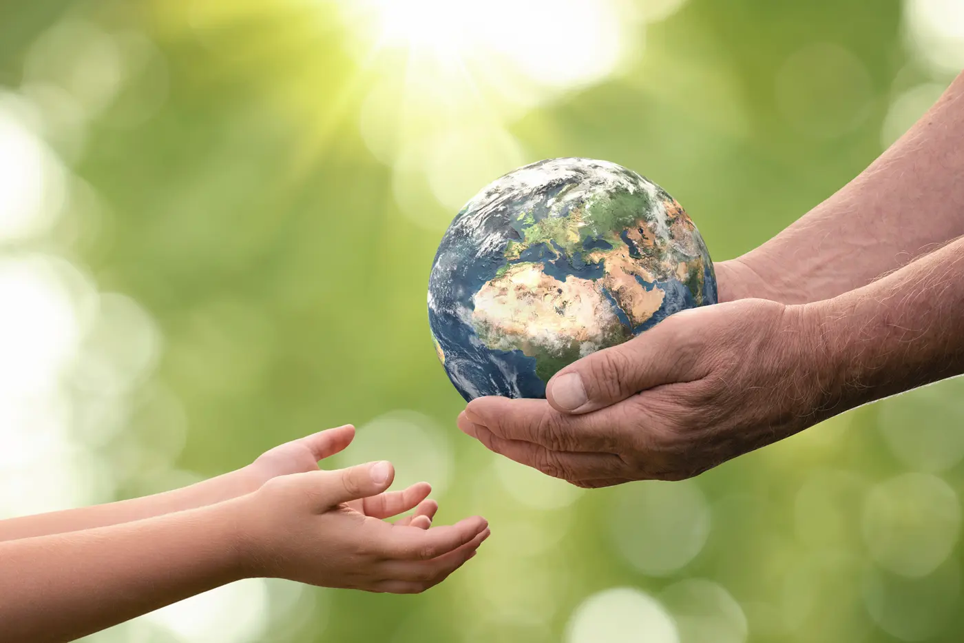 Close up of senior hands giving small planet earth to a child with forest and sunlight in the background