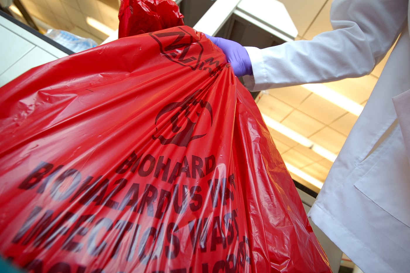 Gloved hand holding red biohazard waste bag
