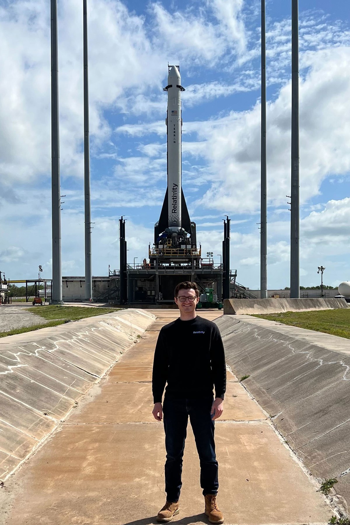 Matt Clancy standing outside in front of a full-sized rocket on a sunny day. 