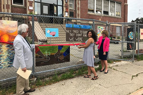 Career Academy student Kiara West cuts the ribbon on an art fence created by students during a day of community service. 