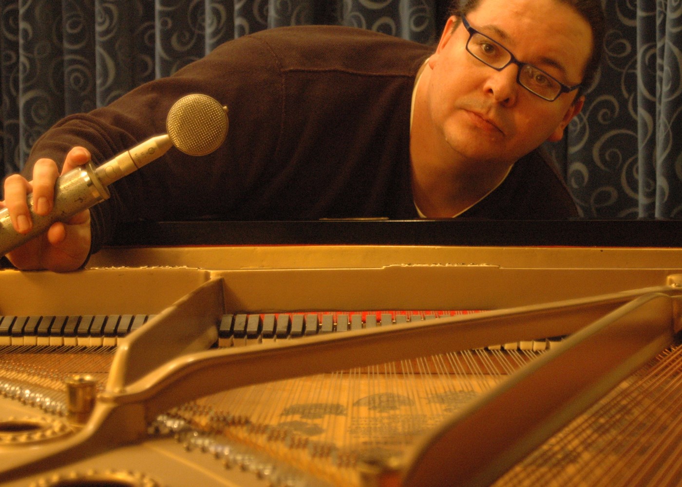 Alexander Case an Associate Professor in the Music Department at UMass Lowell. Here he poses with a microphone inside a piano.