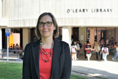 A woman in glasses stands outside in front of a library