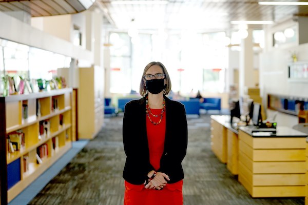 A woman wearing a face covering stands in a library