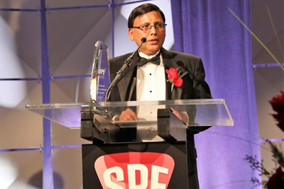 Suresh Shah standing in front of a podium and speaking at an event. 