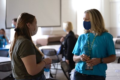 A student in a face covering talks to a woman in a blue tshirt