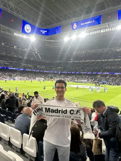 Angelos Boules holds up a Real Madrid C.F. banner at a futbol (soccer) match.